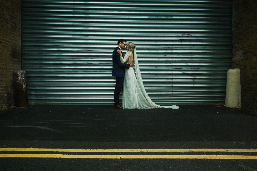 wedding photograph or couple stood against loading bay with yellow lines in foreground