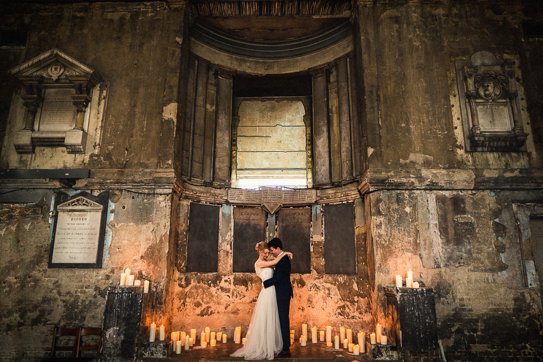 bride and groom in romantic embrace stood on the candlelit stage at the asylum chapel 