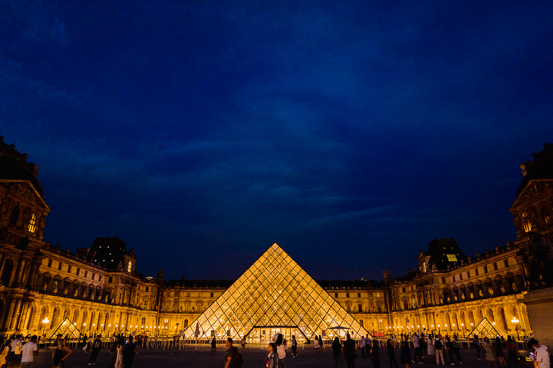 a nighttime scene setting shot of the lit louvre pyramid in Paris 