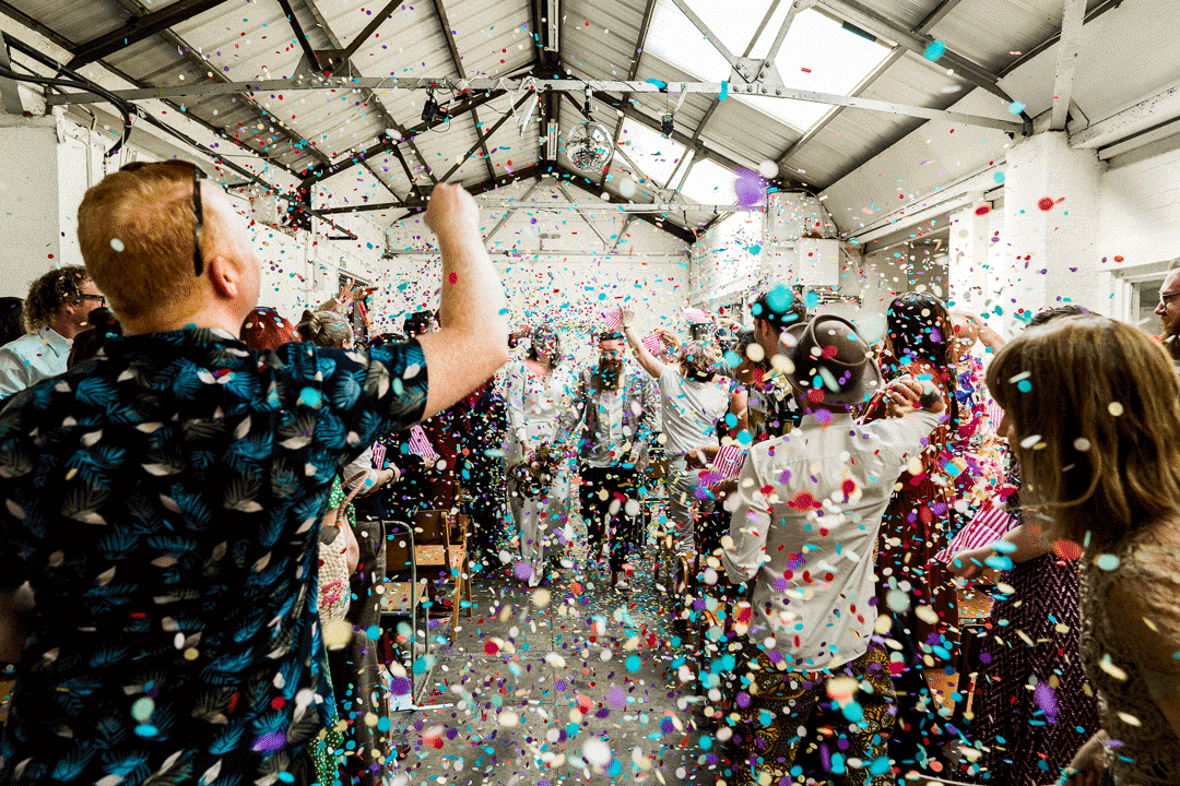 a gif of a bride and groom walking back up the aisle whilst being showered in colourful confetti 