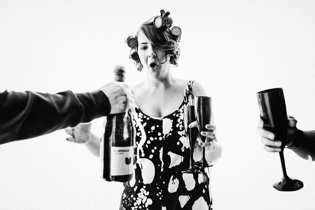 a bridesmaid reacts to a champagne bottle over flowing whilst she awaits with champagne flutes