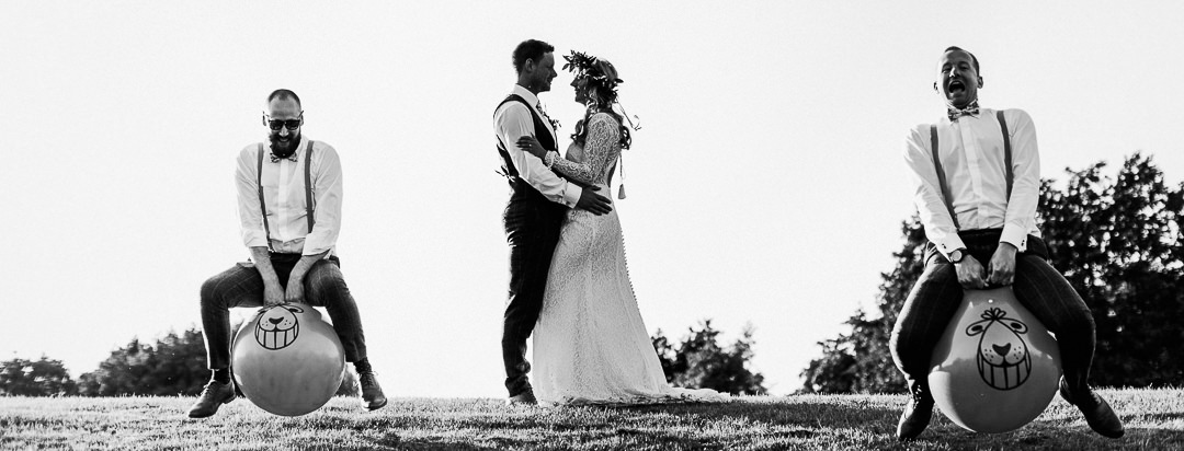 a wedding couple hug as they are photobombed by two wedding guests on space hoppers
