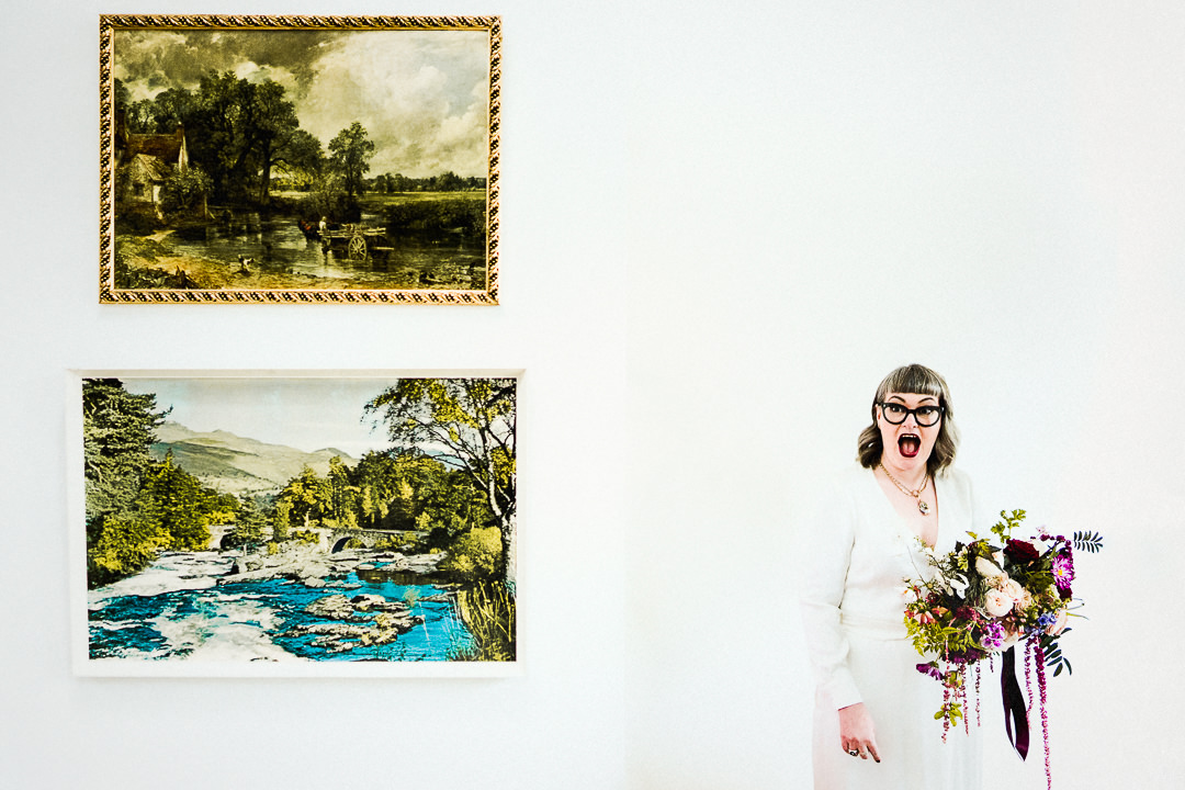 a bride reacts excitedly pre wedding ceremony against a white wall, she is holding her bouquet 