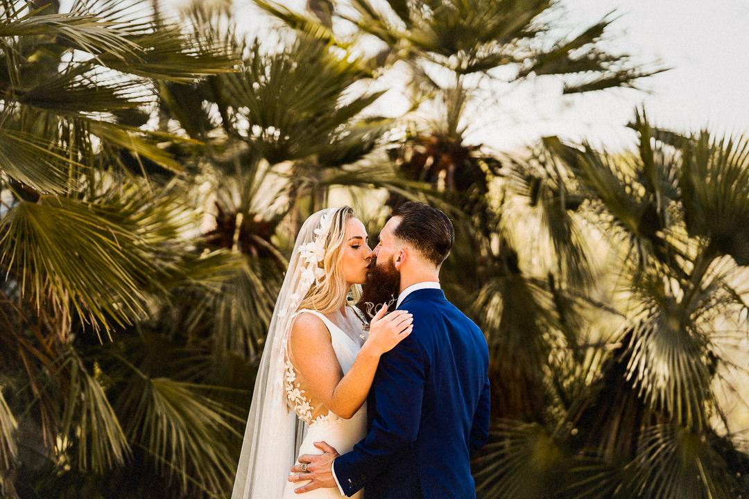 a couple embrace in front of green palms in the village close to cash Felix wedding venue in Spain