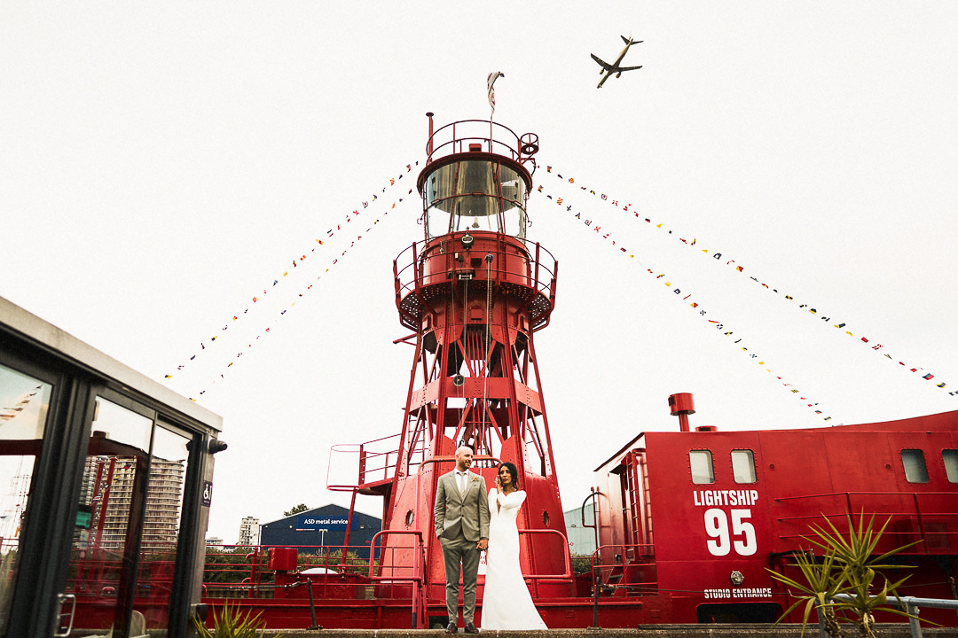 a couple stand next to the lightship at trinity buoy wharf on their wedding day